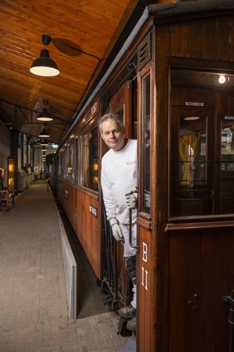 Nol Grasman poseert in een tram. Hij is een oudere man met grijs haar en witte schilderskleding aan. Hij lacht voorzichtig.