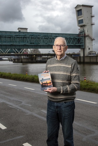 Jan van Wijnen poseert voor een brug in de buurt van Krimpen aan den IJssel. Hij heeft zijn boek vast.