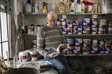 Jan bladert in één van zijn boeken. Hij zit tussen de verfblikken.